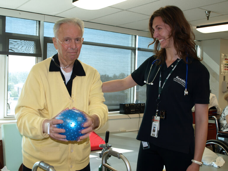 Older male cardia rehabilitation patient works with exercise ball to improve motor skills
