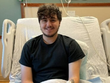Kyle sitting up in his hospital bed smiling with a cast on his left arm.